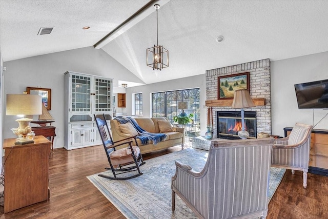 living room with vaulted ceiling with beams, a textured ceiling, a fireplace, wood finished floors, and visible vents