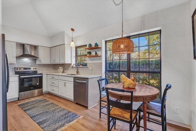 kitchen featuring stainless steel appliances, lofted ceiling, light countertops, a sink, and wall chimney range hood