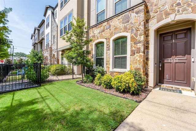 entrance to property with a yard, stone siding, fence, and stucco siding