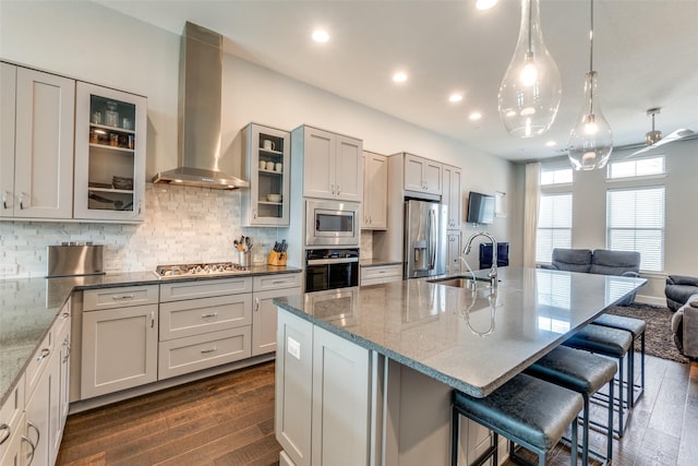 kitchen with tasteful backsplash, appliances with stainless steel finishes, open floor plan, wall chimney range hood, and a sink