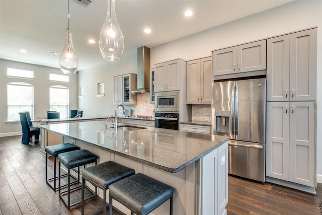 kitchen with a sink, appliances with stainless steel finishes, wall chimney range hood, decorative backsplash, and dark wood-style floors