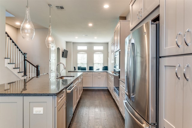 kitchen featuring visible vents, dark stone counters, appliances with stainless steel finishes, dark wood-type flooring, and a sink