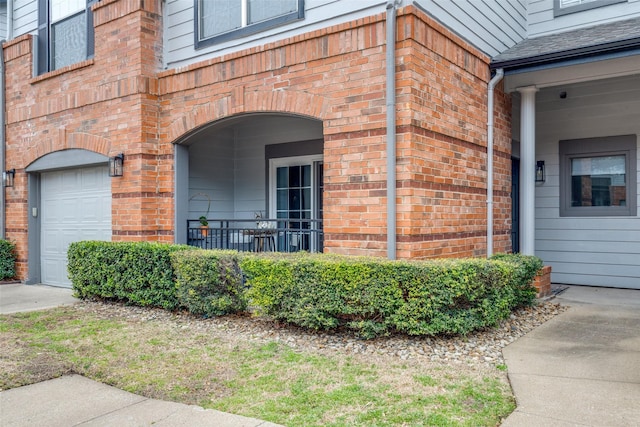 property entrance featuring a shingled roof, brick siding, and a garage