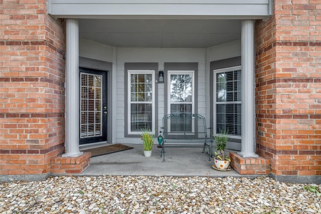 entrance to property featuring a porch and brick siding