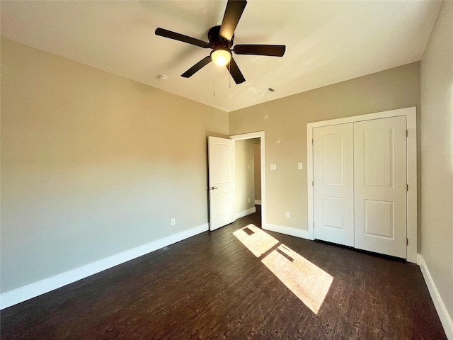 unfurnished bedroom with a closet, dark wood-style flooring, baseboards, and a ceiling fan