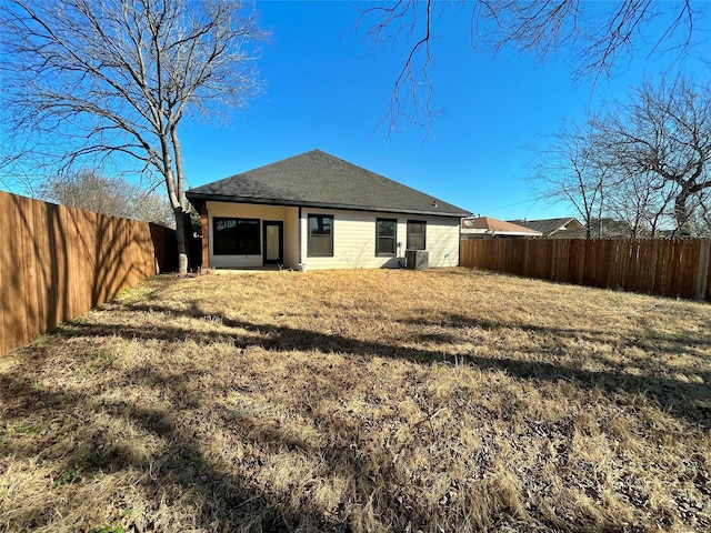 back of house with a fenced backyard, central AC, a shingled roof, and a yard