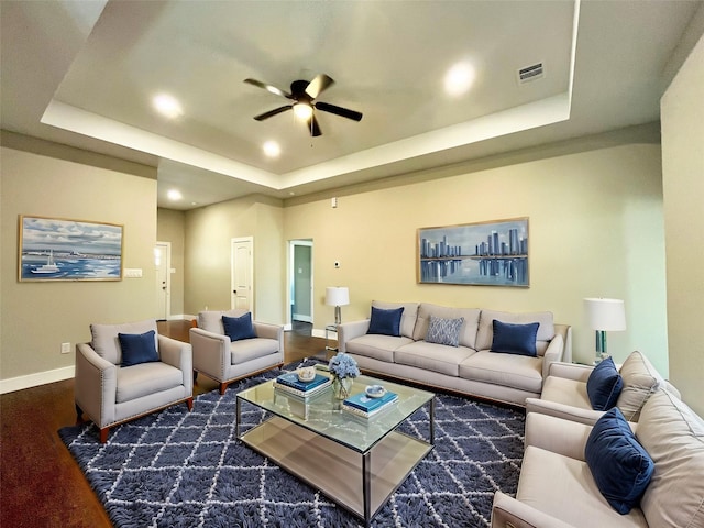 living area featuring ceiling fan, wood finished floors, visible vents, baseboards, and a raised ceiling