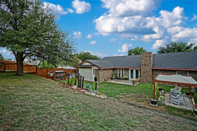 rear view of house with a fenced backyard, brick siding, roof with shingles, a lawn, and a patio area