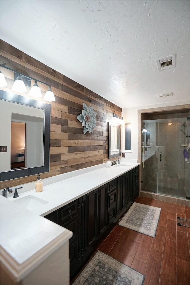 full bathroom with a sink, visible vents, a shower stall, wood tiled floor, and double vanity