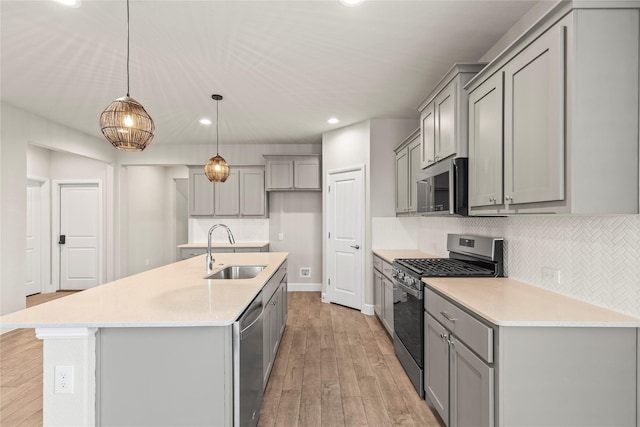 kitchen with decorative backsplash, appliances with stainless steel finishes, gray cabinetry, light wood-style floors, and a sink