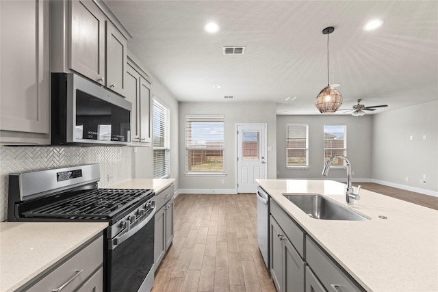 kitchen featuring gray cabinetry, a sink, visible vents, appliances with stainless steel finishes, and decorative backsplash