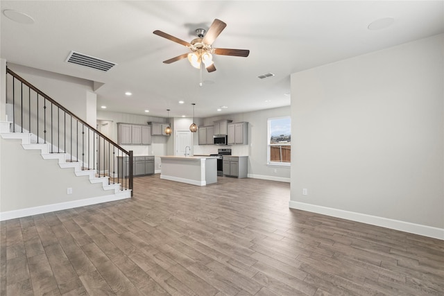 unfurnished living room featuring stairs, visible vents, ceiling fan, and wood finished floors