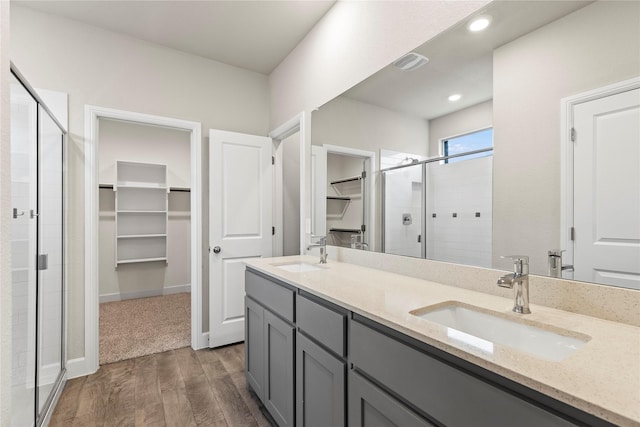 bathroom with wood finished floors, a stall shower, a sink, and a walk in closet