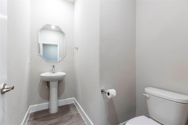 half bathroom with toilet, baseboards, and wood finished floors