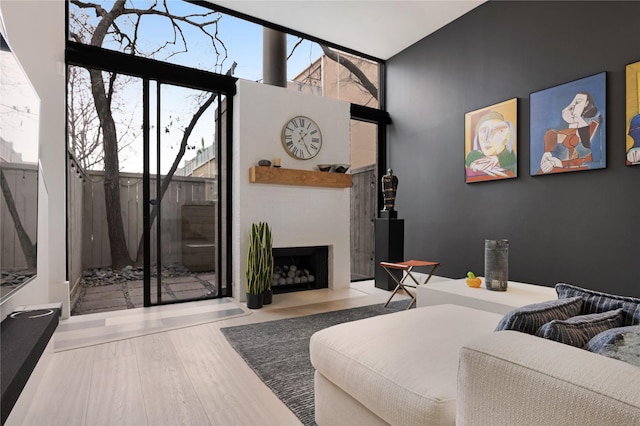 bedroom featuring a fireplace with flush hearth, wood finished floors, access to outside, a high ceiling, and a wall of windows