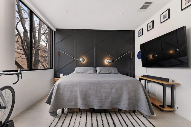 bedroom featuring light wood-style flooring, visible vents, and a decorative wall