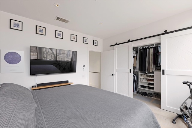 bedroom featuring a barn door, visible vents, light wood-style flooring, and a closet