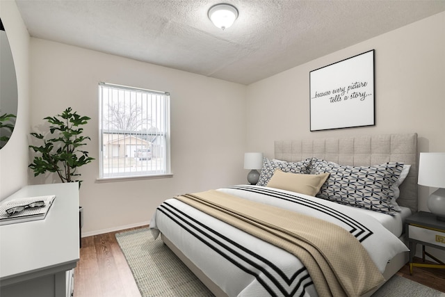 bedroom with a textured ceiling, baseboards, and wood finished floors