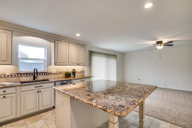 kitchen with cream cabinetry, light colored carpet, decorative backsplash, a sink, and light stone countertops