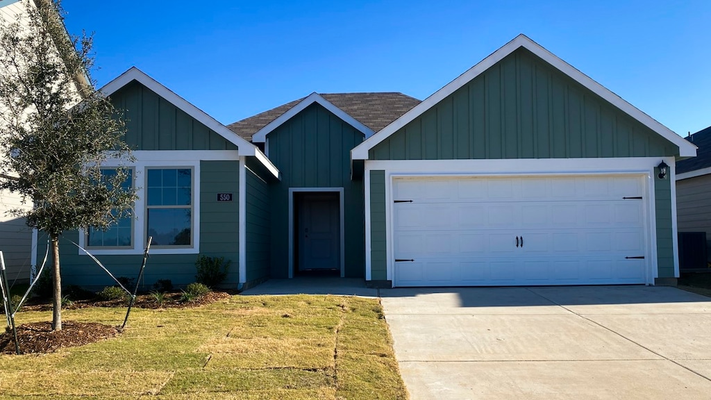 ranch-style house with an attached garage, concrete driveway, roof with shingles, a front lawn, and board and batten siding