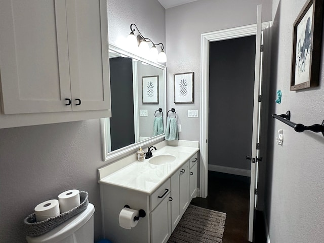 half bath with toilet, a textured wall, baseboards, and vanity