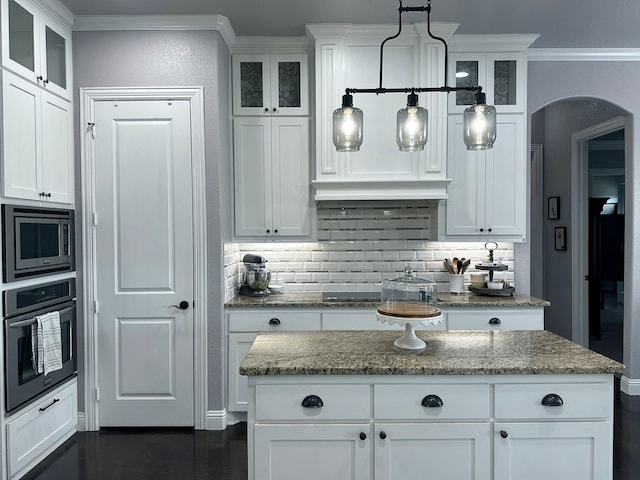 kitchen with wall oven, arched walkways, stainless steel microwave, ornamental molding, and white cabinetry