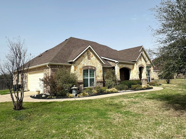 french country style house featuring an attached garage, a shingled roof, brick siding, driveway, and a front lawn