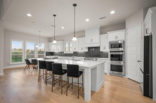 kitchen featuring stainless steel appliances, a sink, light countertops, backsplash, and light wood finished floors