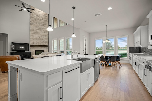 kitchen with a center island with sink, visible vents, stainless steel dishwasher, light wood-style floors, and a stone fireplace