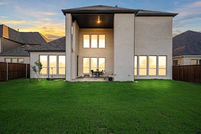 back of property at dusk featuring brick siding, a yard, and a fenced backyard