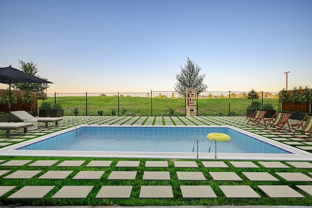 pool at dusk featuring a fenced backyard, a yard, and a community pool