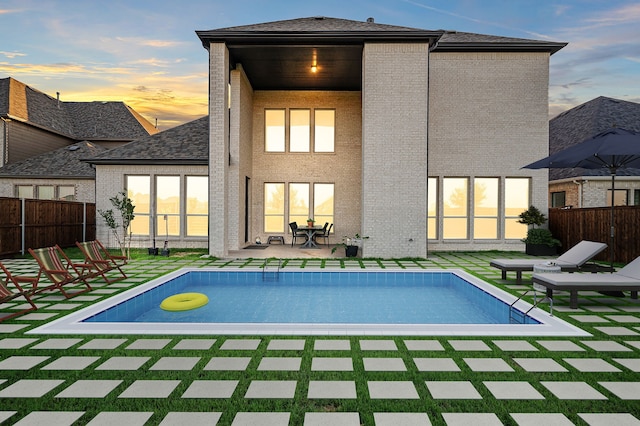 back of house at dusk featuring brick siding, fence, a fenced in pool, and a patio