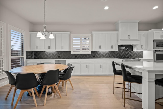 kitchen with light wood finished floors, a kitchen breakfast bar, stainless steel appliances, light countertops, and white cabinetry