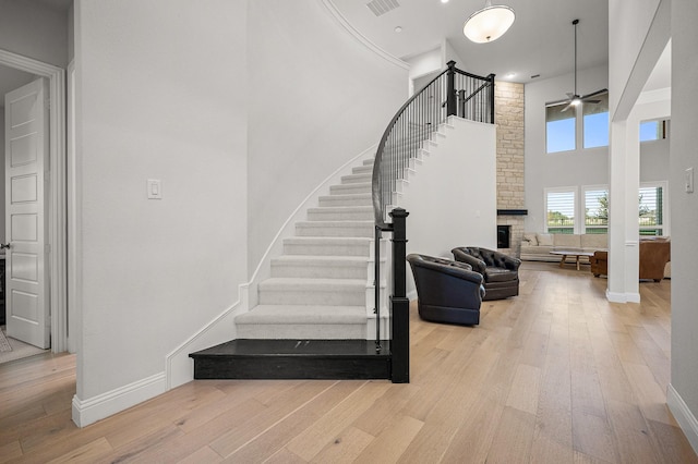 stairs with a stone fireplace, a towering ceiling, baseboards, a ceiling fan, and wood-type flooring