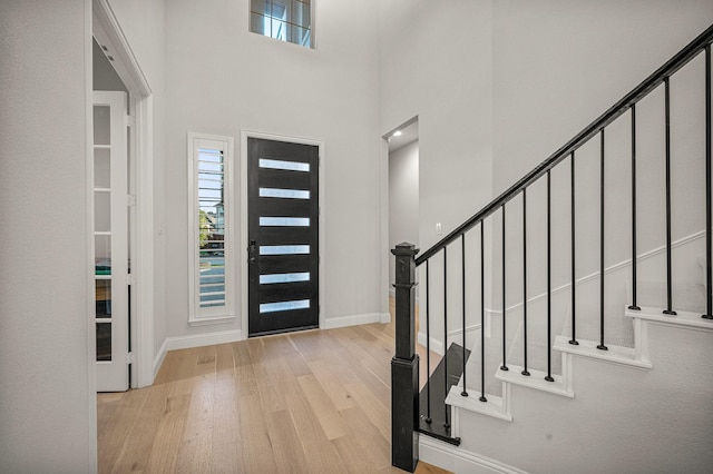 foyer with a towering ceiling, stairway, baseboards, and wood finished floors