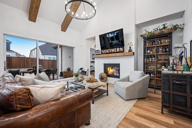 living area featuring beam ceiling, a chandelier, a glass covered fireplace, wood finished floors, and high vaulted ceiling