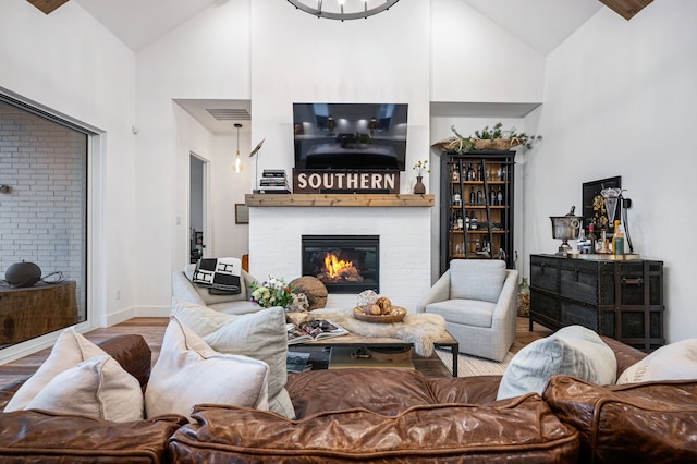 living area with visible vents, a glass covered fireplace, wood finished floors, high vaulted ceiling, and baseboards