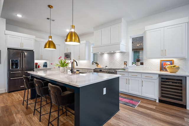 kitchen with beverage cooler, a kitchen breakfast bar, stainless steel appliances, light wood-style floors, and a sink