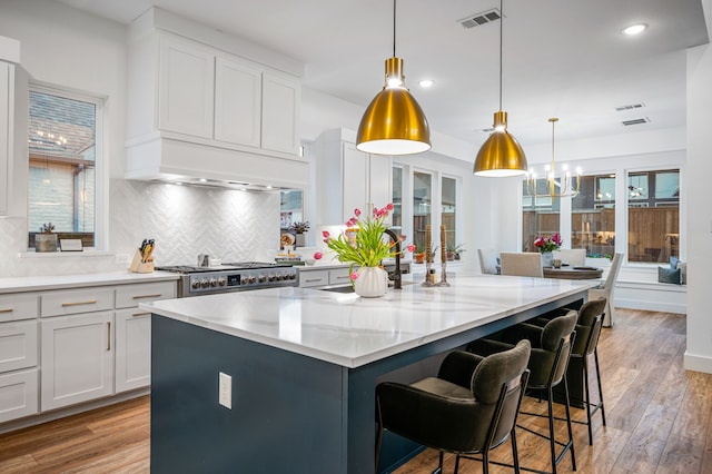 kitchen featuring visible vents, custom range hood, a kitchen island, stainless steel gas range, and light wood-type flooring