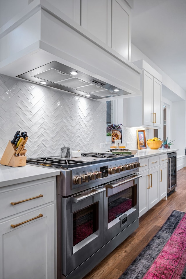 kitchen with range with two ovens, beverage cooler, premium range hood, white cabinets, and light countertops