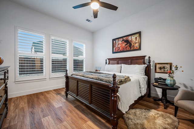 bedroom with a ceiling fan, wood finished floors, visible vents, and baseboards