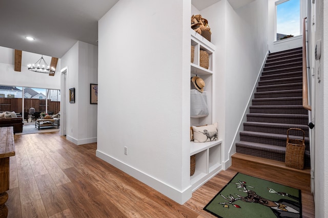 hallway with a wealth of natural light, stairs, a chandelier, and wood finished floors