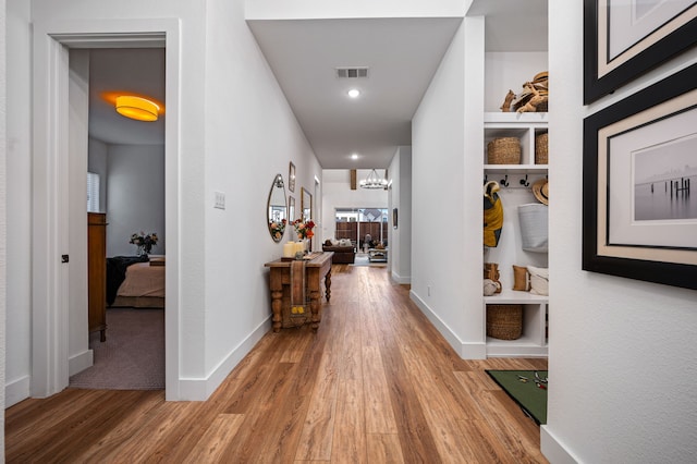 hallway featuring built in features, baseboards, visible vents, and wood finished floors