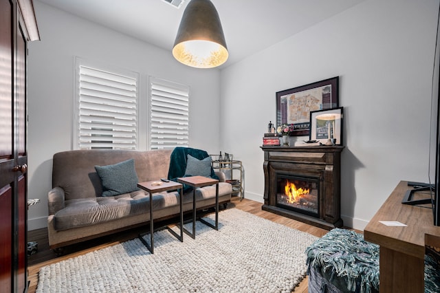 living area with baseboards, wood finished floors, and a glass covered fireplace