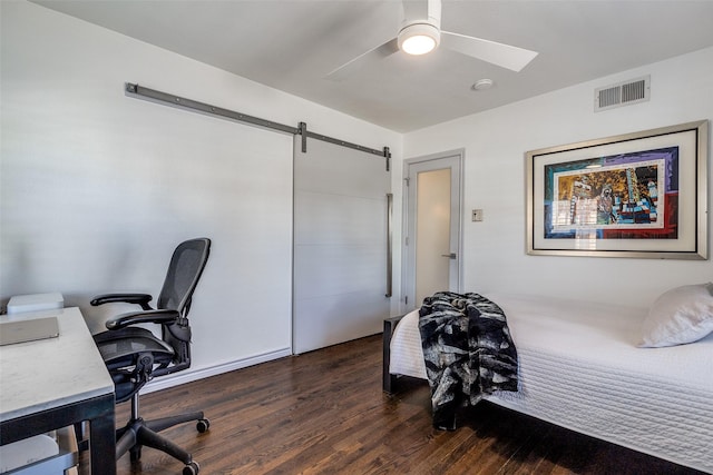 bedroom featuring dark wood finished floors, visible vents, a barn door, and a ceiling fan