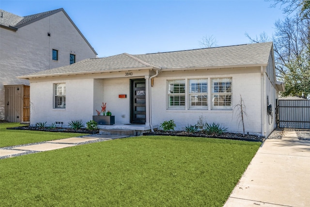 view of front of house with a front yard, a gate, brick siding, and a shingled roof