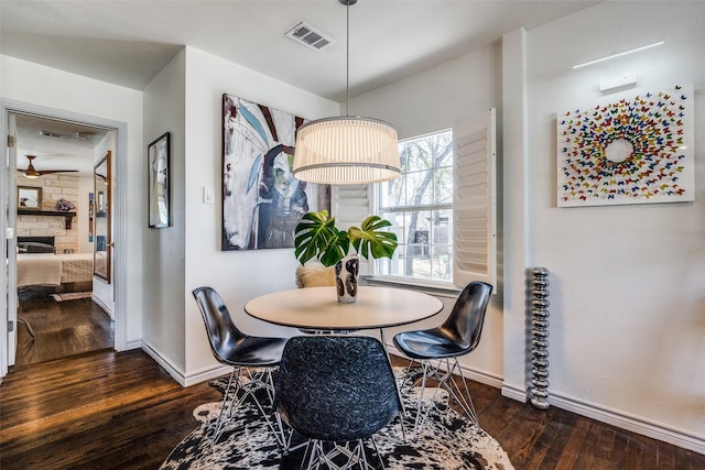 dining area featuring visible vents, baseboards, dark wood-type flooring, and a stone fireplace