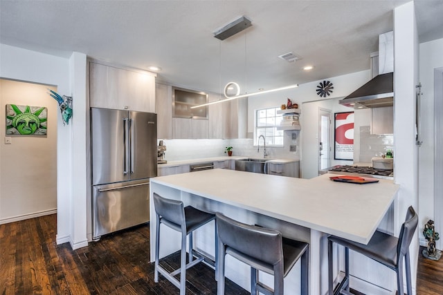 kitchen featuring a breakfast bar, stainless steel appliances, decorative backsplash, light countertops, and wall chimney exhaust hood