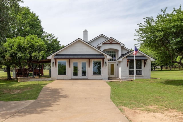 view of front of house with a standing seam roof, a chimney, a front lawn, and brick siding