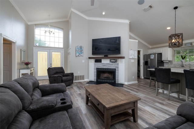 living room with an inviting chandelier, light wood-style flooring, visible vents, and ornamental molding